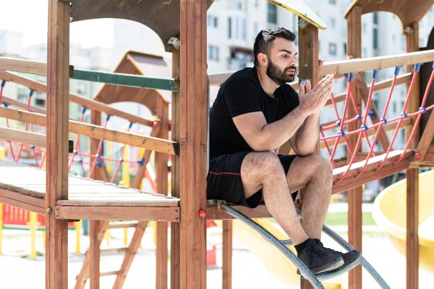 Jovem apto bonito homem adulto descansando ao ar livre no parque infantil