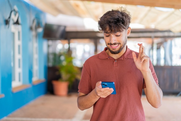 Foto jovem árabe bonito ao ar livre usando telefone celular com os dedos cruzados