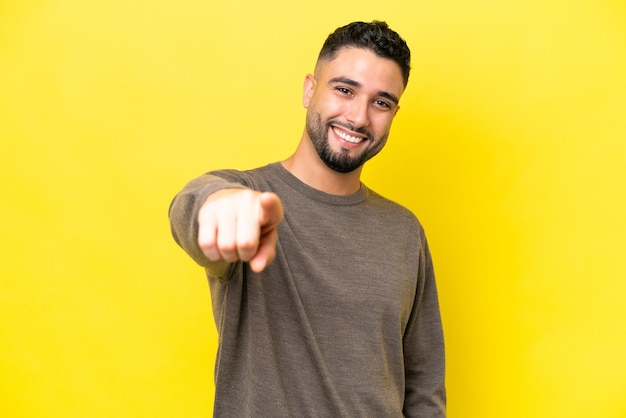 Jovem árabe bonito isolado em fundo amarelo apontando para a frente com expressão feliz