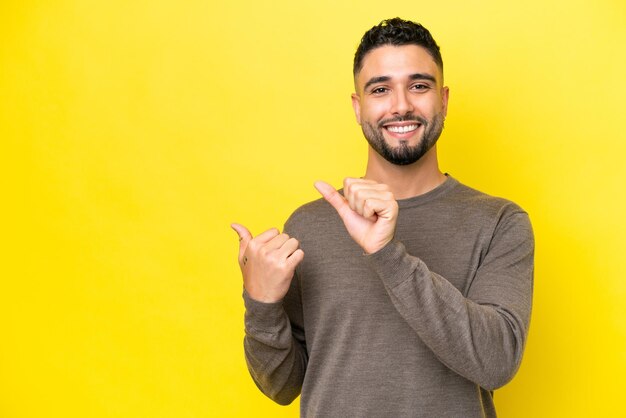 Jovem árabe bonito isolado em fundo amarelo apontando para o lado para apresentar um produto