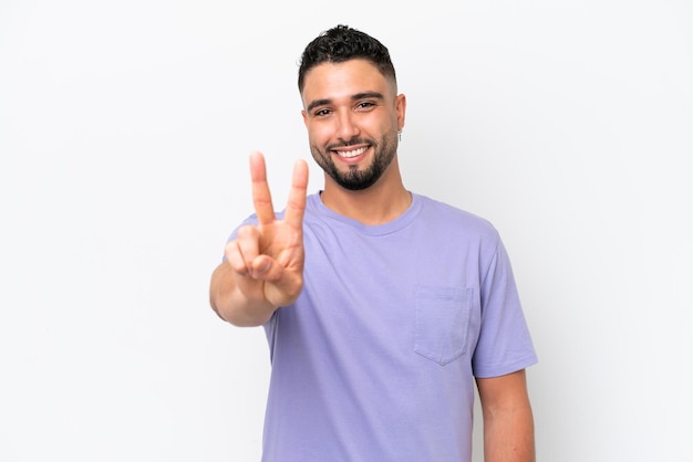 Jovem árabe bonito isolado no fundo branco sorrindo e mostrando sinal de vitória