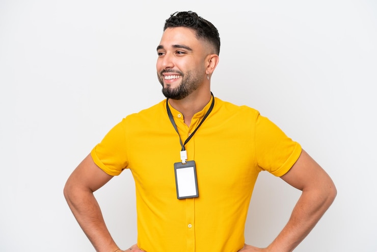 Foto jovem árabe com cartão de identificação isolado no fundo branco posando com os braços no quadril e sorrindo