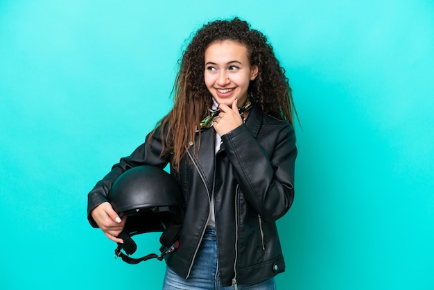 Jovem árabe com um capacete de moto isolado em fundo azul olhando para o lado e sorrindo