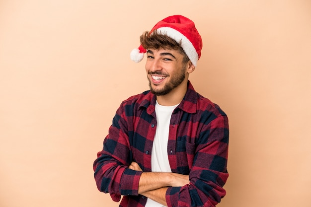 Jovem árabe comemorando o natal isolado em um fundo bege, rindo e se divertindo.