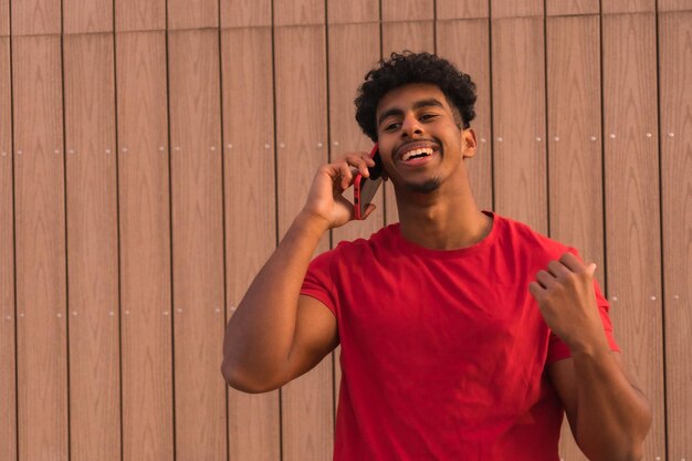 Jovem árabe de camiseta vermelha em um fundo de madeira sorrindo falando ao telefone
