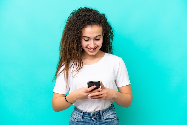 Jovem árabe isolada em fundo azul enviando uma mensagem ou e-mail com o celular