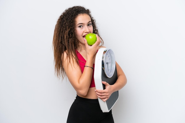 Foto jovem árabe isolada em fundo branco com máquina de pesagem e com uma maçã