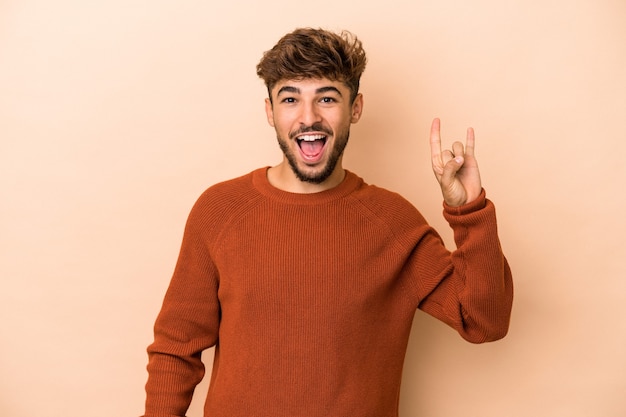 Jovem árabe isolado em um fundo bege, mostrando um gesto de chifres como um conceito de revolução.