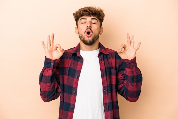 Jovem árabe isolado em um fundo bege relaxa após um árduo dia de trabalho, ela está realizando ioga.