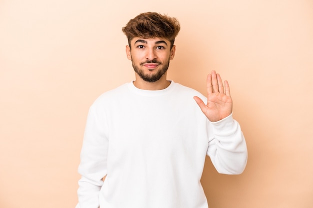 Jovem árabe isolado em um fundo bege, sorrindo alegre mostrando o número cinco com os dedos.