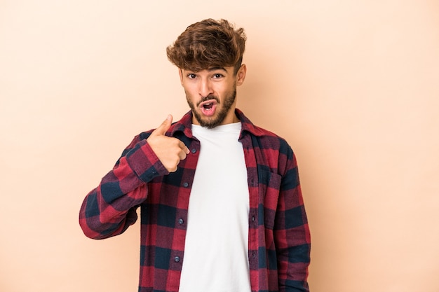 Jovem árabe isolado em um fundo bege surpreso apontando com o dedo, sorrindo amplamente.