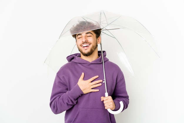 Jovem árabe segurando um guarda-chuva ri alto, mantendo a mão no peito.