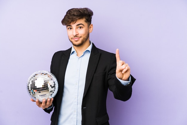 Jovem árabe segurando uma bola de festa isolada mostrando o número um com o dedo.