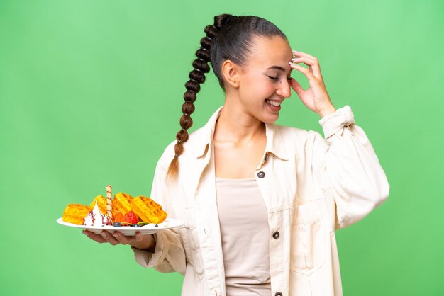 Jovem árabe segurando waffles sobre fundo isolado rindo