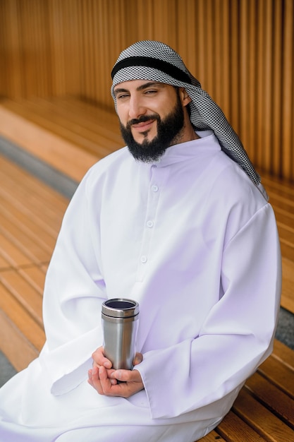 Jovem árabe sentado em um banco de madeira com metal
