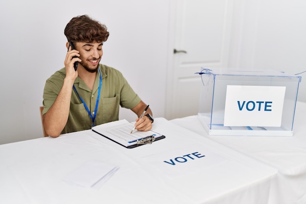 Jovem árabe sorrindo confiante falando no smartphone no colégio eleitoral