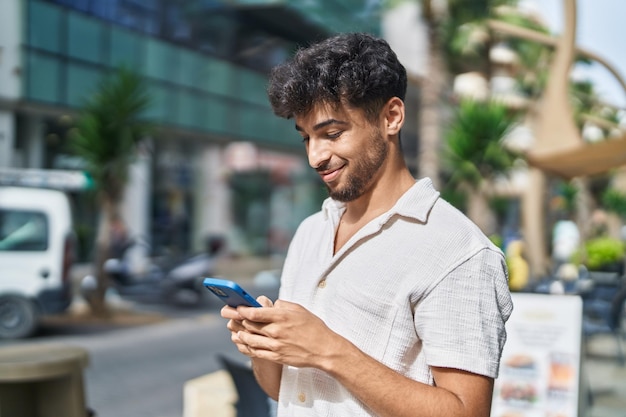 Jovem árabe sorrindo confiante usando smartphone na rua