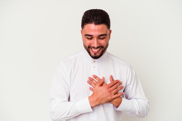 Jovem árabe vestindo roupas típicas árabes, isoladas no fundo branco, rindo, mantendo as mãos no coração, o conceito de felicidade.