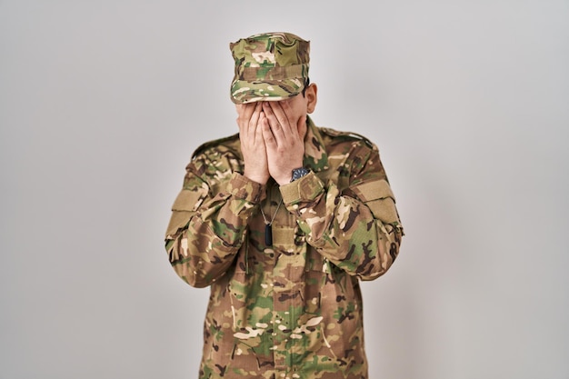 Jovem árabe vestindo uniforme do exército de camuflagem com expressão triste cobrindo o rosto com as mãos enquanto chorava. conceito de depressão.