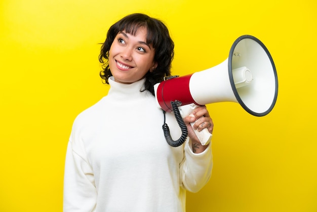 Jovem argentina isolada em fundo amarelo segurando um megafone e olhando para cima enquanto sorria