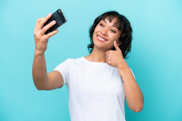 Jovem argentina isolada em fundo azul fazendo uma selfie com telefone celular