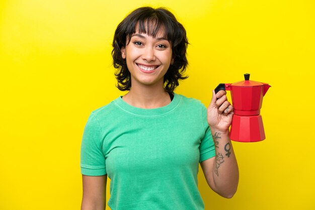 Jovem argentina segurando cafeteira isolada em fundo amarelo sorrindo muito