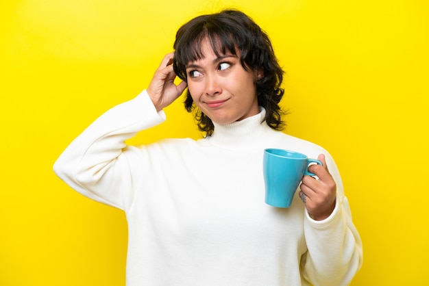 Jovem argentina segurando uma xícara de café isolada em fundo amarelo com dúvidas e com expressão facial confusa