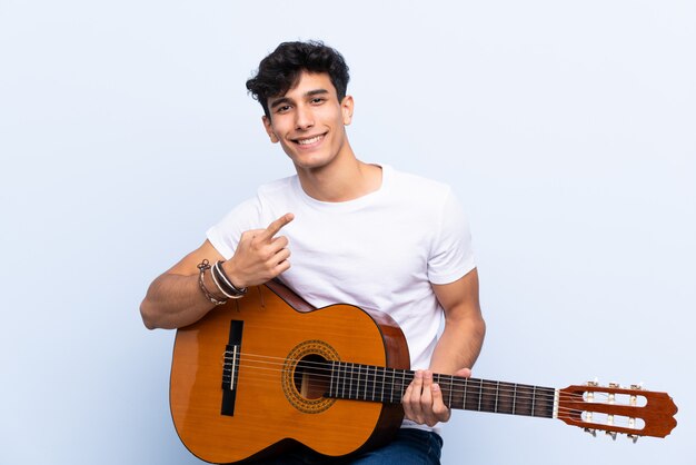 Jovem argentino com guitarra apontando para o lado para apresentar um produto
