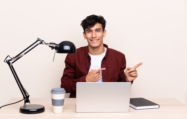 Jovem argentino em uma mesa com um laptop em seu local de trabalho, apontando o dedo para o lado