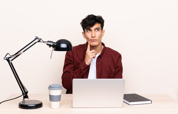 Jovem argentino em uma mesa com um laptop em seu local de trabalho, pensando em uma idéia