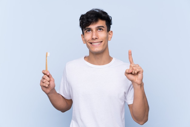 Jovem argentino escovando os dentes sobre parede azul isolada, com a intenção de perceber a solução enquanto levanta um dedo