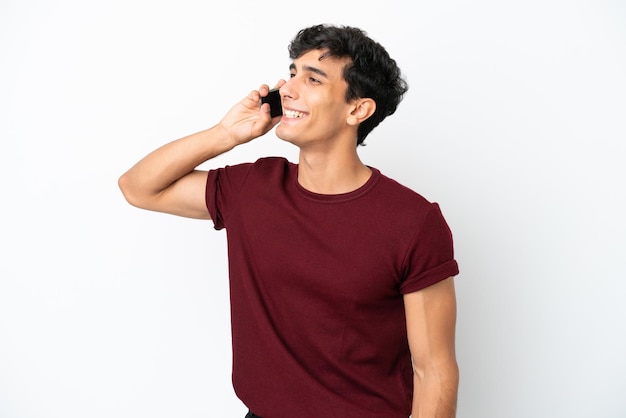 Jovem argentino isolado em fundo branco mantendo uma conversa com o celular