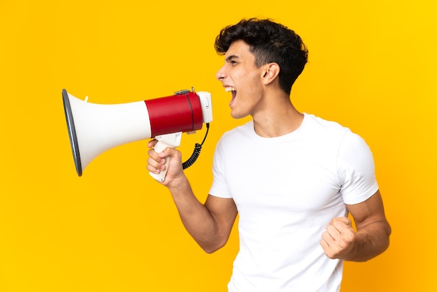 Jovem argentino isolado em um fundo amarelo gritando em um megafone para anunciar algo em posição lateral