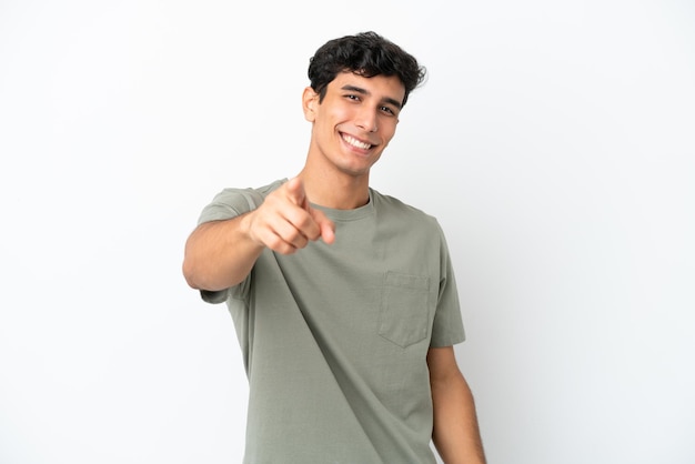 Jovem argentino isolado em um fundo branco apontando para a frente com uma expressão feliz