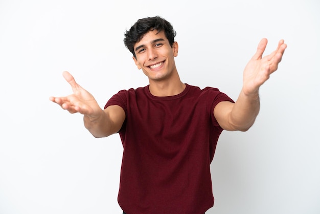 Jovem argentino isolado em um fundo branco apresentando e convidando para vir com a mão