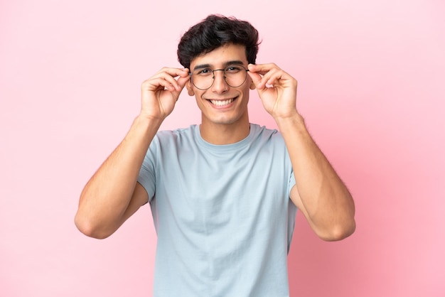 Jovem argentino isolado no fundo rosa com óculos com expressão feliz