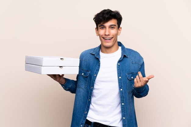 Jovem argentino segurando pizzas sobre parede isolada com expressão facial chocado