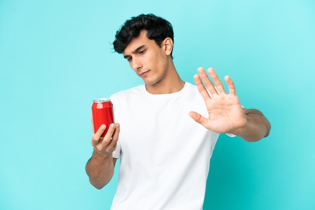 Jovem argentino segurando um refresco isolado em fundo azul fazendo gesto de parada e desapontado