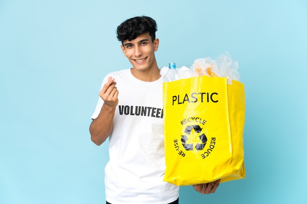 Jovem argentino segurando uma sacola cheia de plástico fazendo gesto de dinheiro
