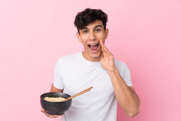 Jovem argentino sobre parede branca isolada, gritando com a boca aberta, segurando uma tigela de macarrão com pauzinhos