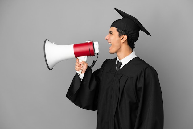 Jovem argentino universitário isolado em um fundo cinza gritando em um megafone