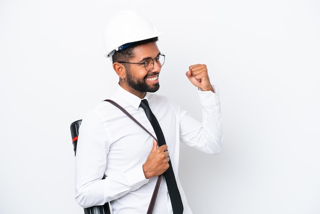 Jovem arquiteto brasileiro com capacete e segurando plantas isoladas no fundo branco comemorando uma vitória