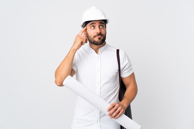 Jovem arquiteto com capacete e segurando plantas isoladas em branco, tendo dúvidas e pensando