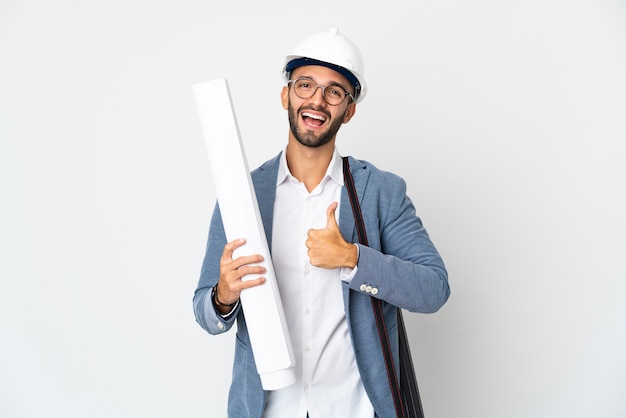 Jovem arquiteto com capacete e segurando plantas isoladas no fundo branco fazendo um gesto de polegar para cima