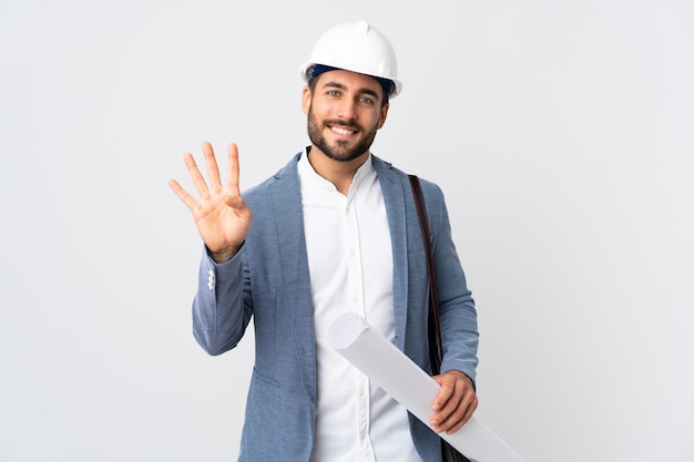 Jovem arquiteto com capacete e segurando plantas isoladas no fundo branco feliz e contando quatro com os dedos