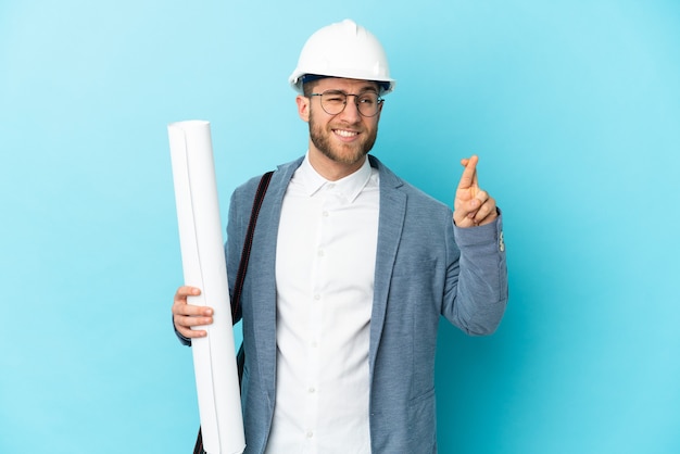 Jovem arquiteto com capacete segurando plantas com os dedos se cruzando e desejando o melhor