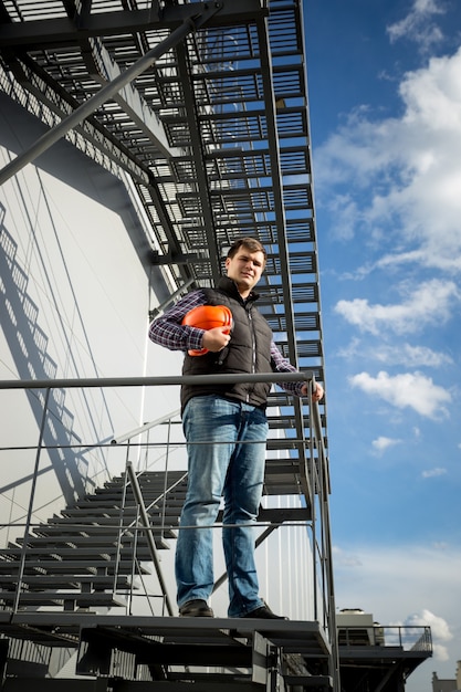 Jovem arquiteto em pé na escada de metal ao lado da fábrica