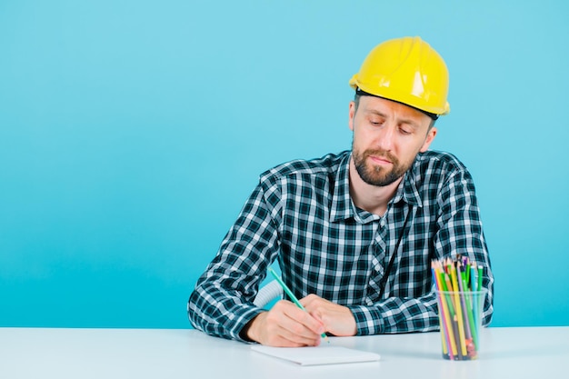 Jovem arquiteto está escrevendo sentado no fundo azul