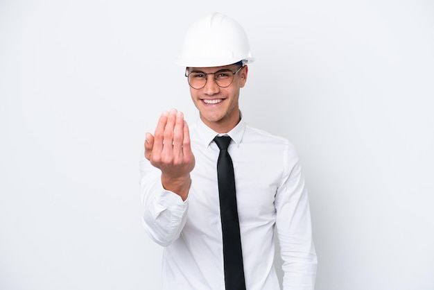 Jovem arquiteto homem caucasiano com capacete e segurando plantas isoladas no fundo branco convidando para vir com a mão Feliz por você ter vindo