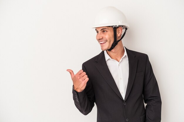 Foto jovem arquiteto homem caucasiano isolado no fundo branco aponta com o dedo polegar afastado, rindo e despreocupado.